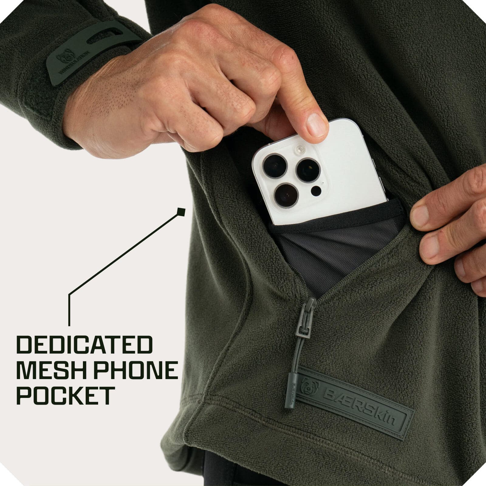 Person placing a phone into a zippered mesh chest pocket on a green Baerskin fleece jacket