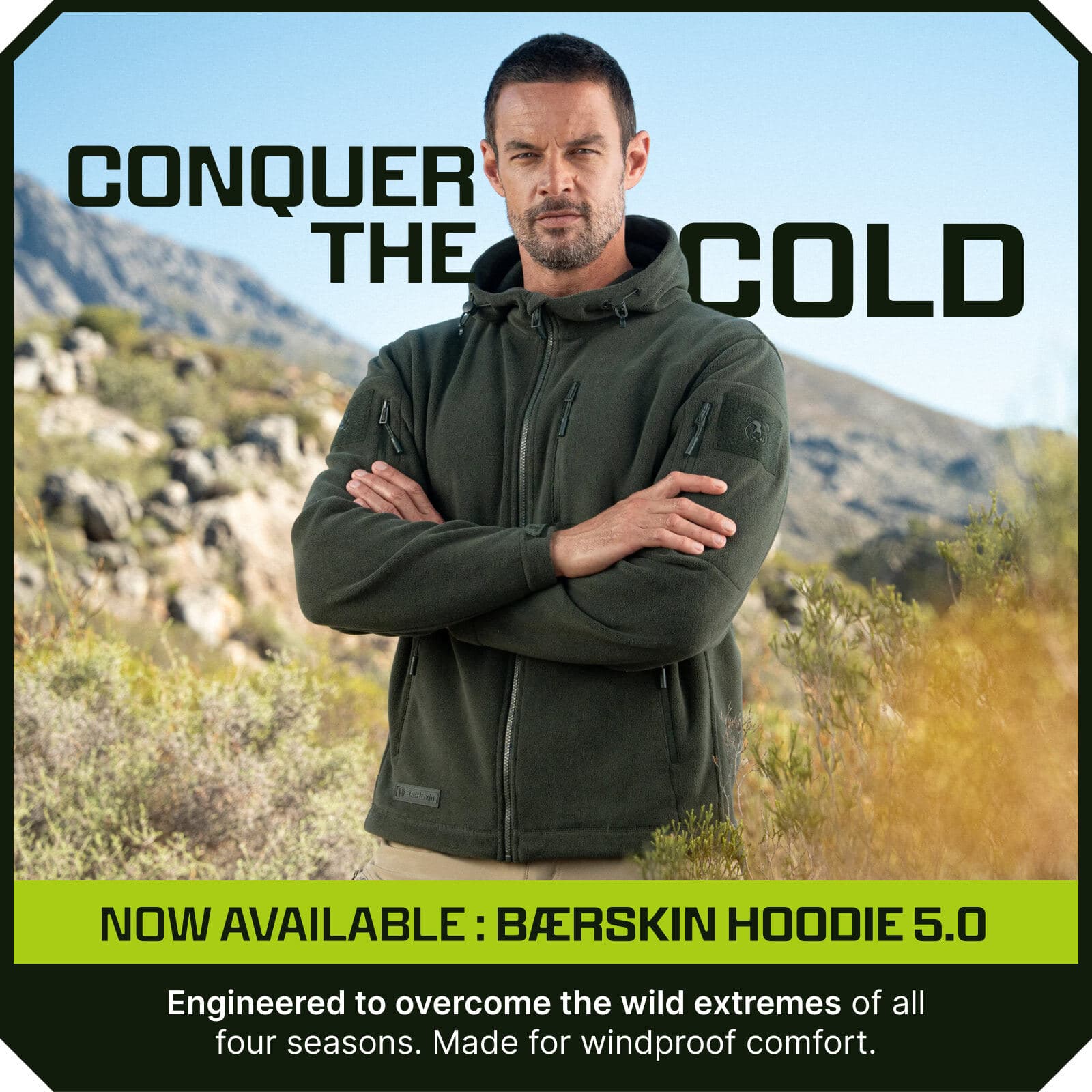 Man wearing an olive green zip-up fleece hoodie with chest and sleeve pockets, arms crossed, standing outdoors in mountains